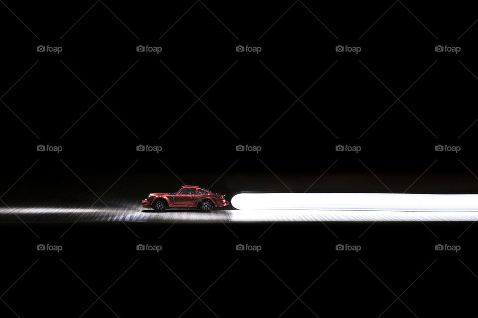 A portrait of a red toy sportscar with some light painting done around it implying motion.