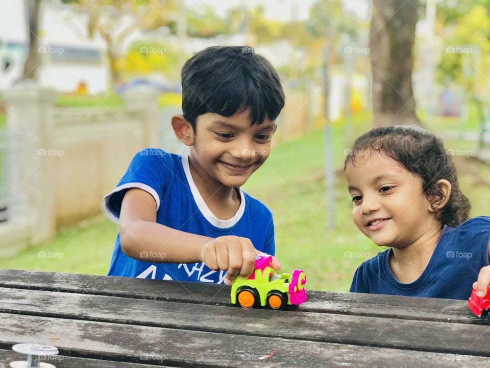 A boy and girl both are having cute smile on their faces and they playing outdoor with toy cars.