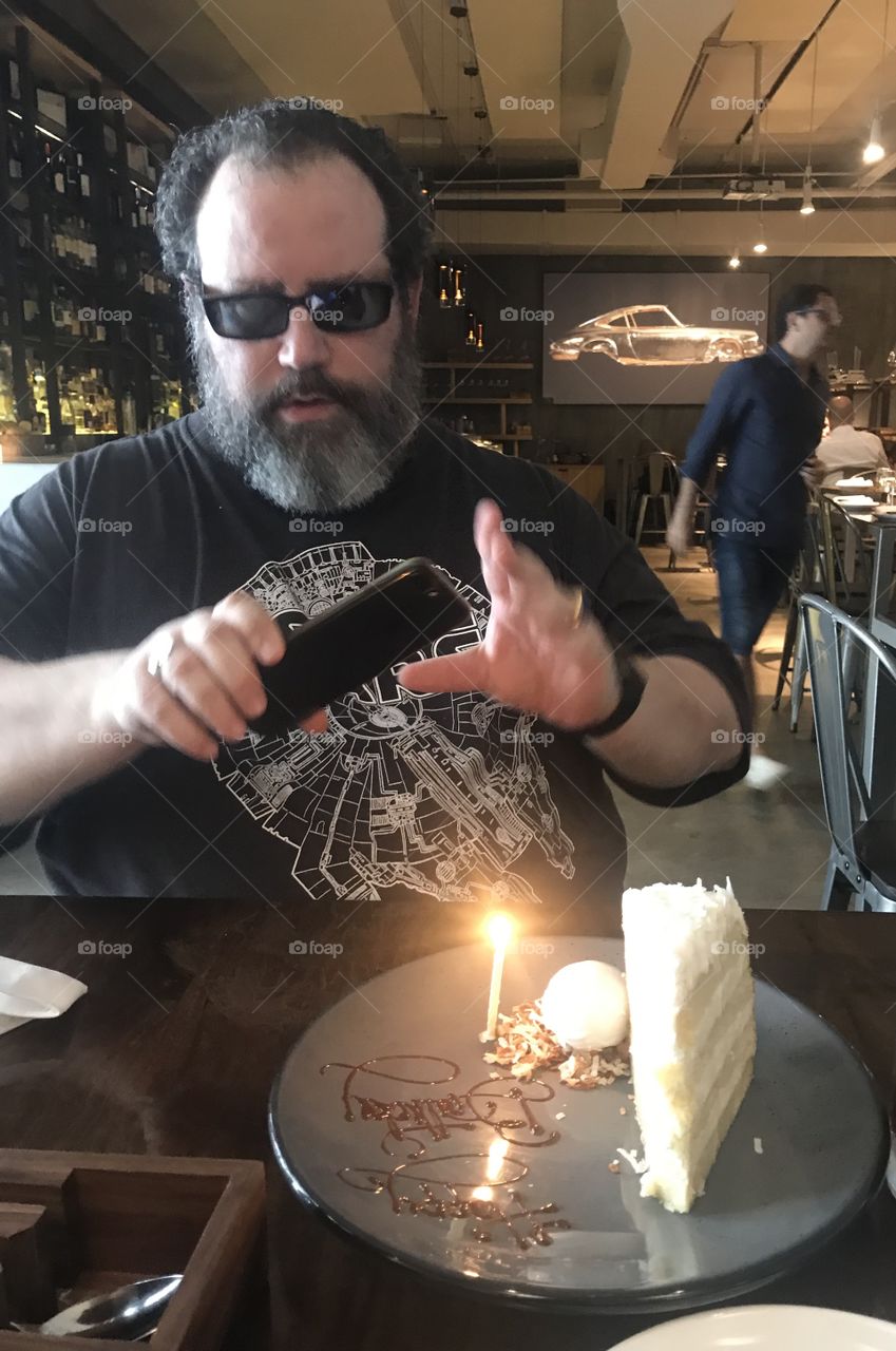Man( my brother) long beard, taking pictures of his birthday cake 