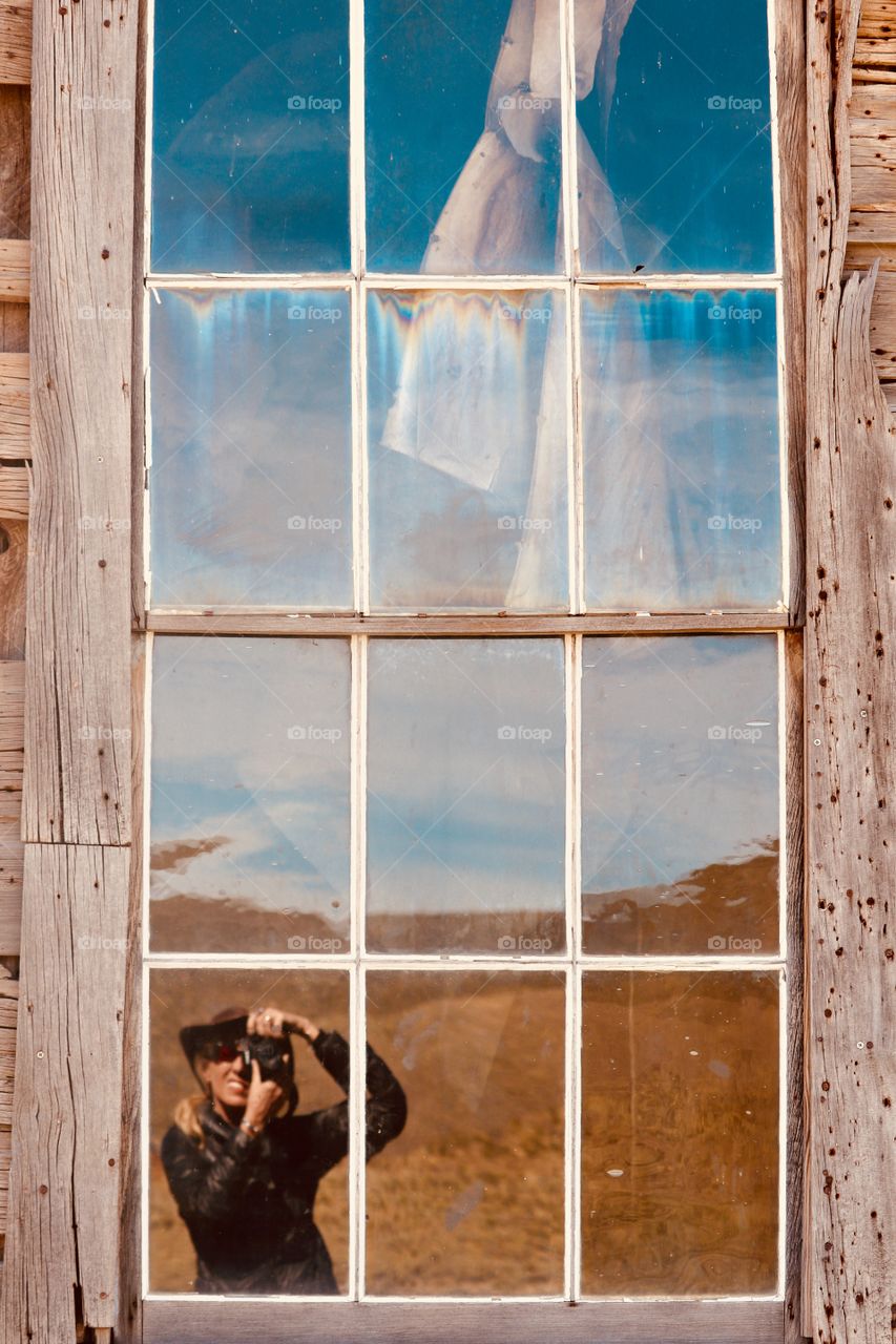 Reflection of photographer (female) in window of old abandoned home in the desert