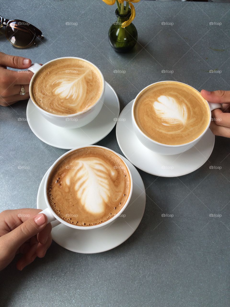 Three friends, chatting over beautiful honey lattes. Creamy latter art designs, each unique and intricate. 