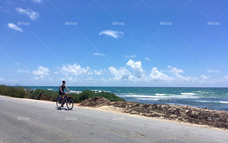 A biker rides down the road alongside a blue ocean in Tulum, Mexico. 