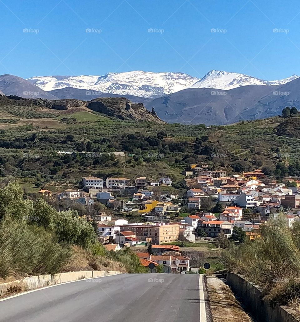 A route leads down to a small down and the snow capped Spanish Sierra Nevada peaks in the far distance.