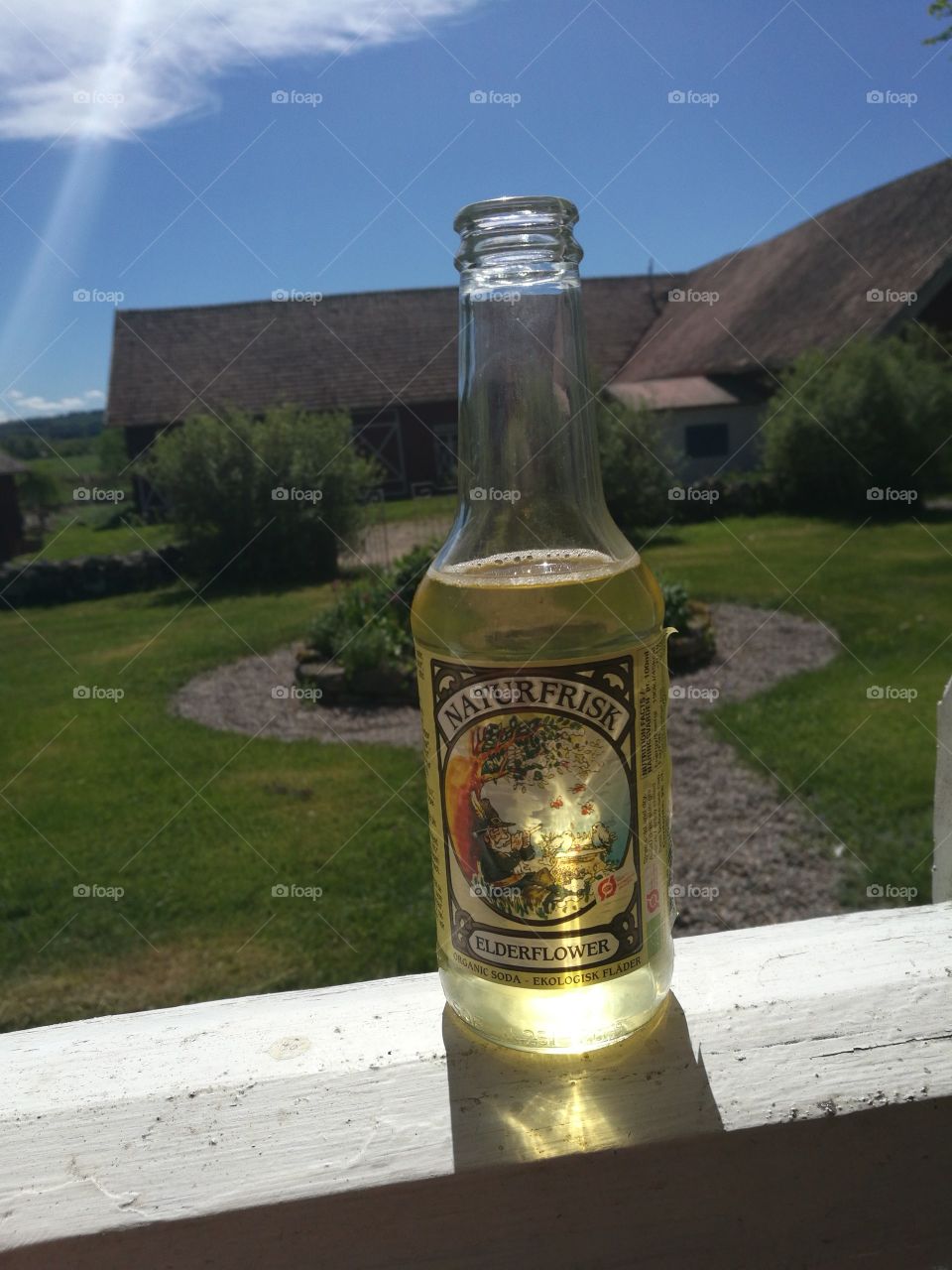 pic of a organic soda whit eldflower taste. in the backrond my grandmother and grandfathers yard in sweden.