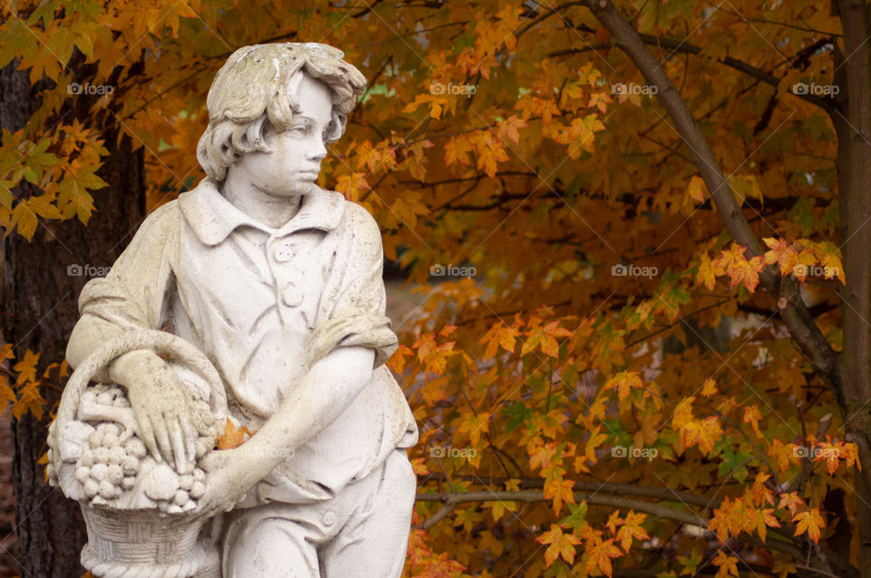 plaster statue of a boy on a background of yellow autumn leaves in the park