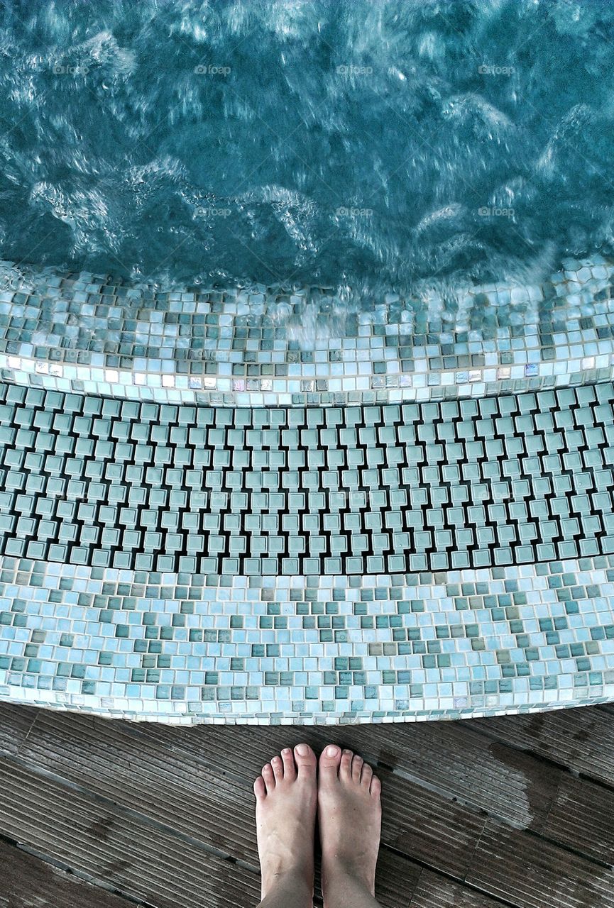Looking down at swimming pool. Female feet standing at the age of a swimming pool