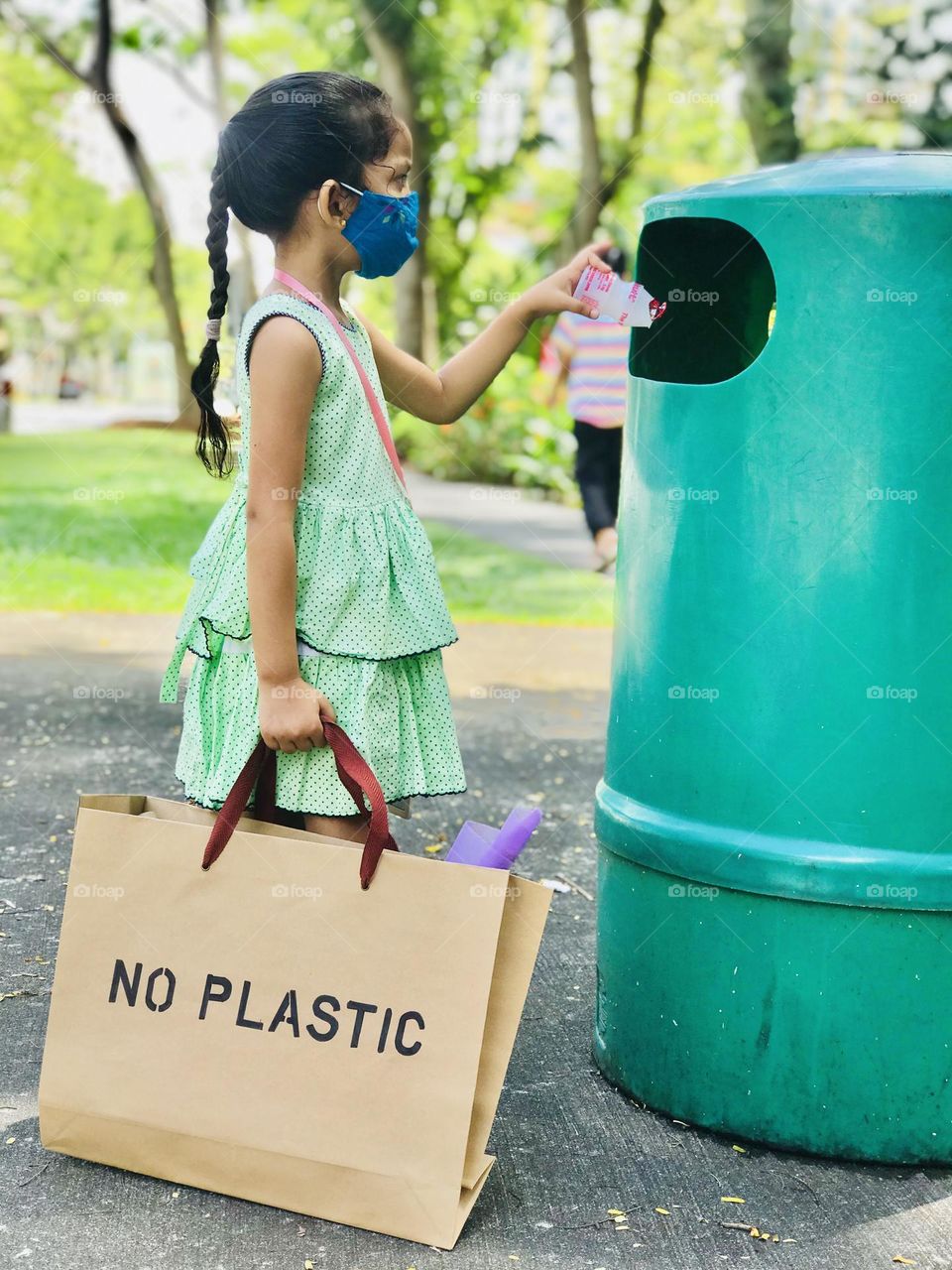 Kid’s learn about advantages of using paper bags and disadvantages of using plastic.here a four year old girl throwing a plastic drink bottle into dustbin and holding a paper bag.