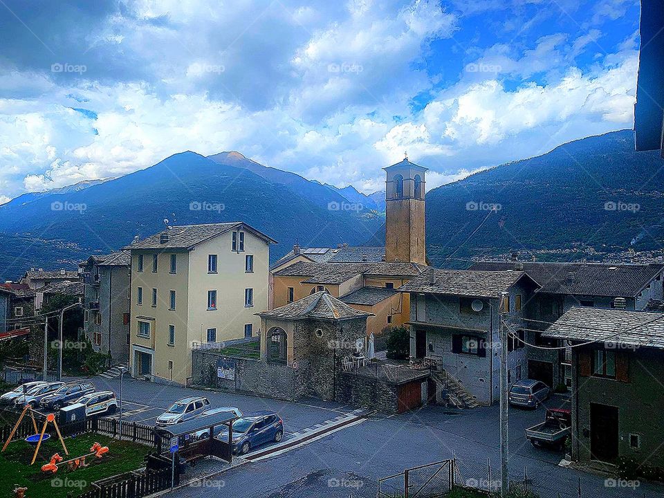 Village. View of the small settlement of Faedo Valtellino. Italy. In the background are the Alps mountains that touch the blue sky with white-gray clouds.
