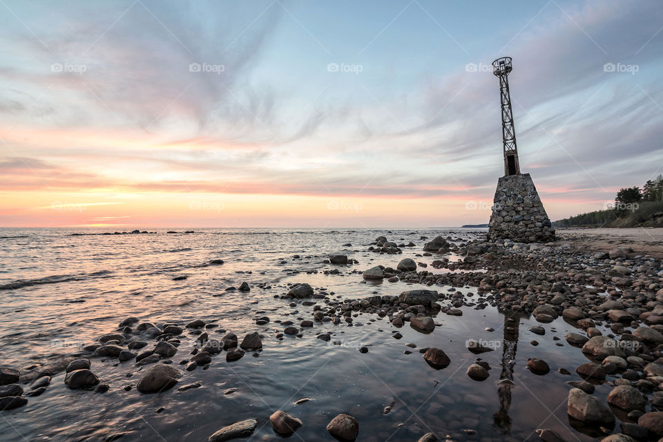 Old lighthouse, rocky beach at sunset hour.
