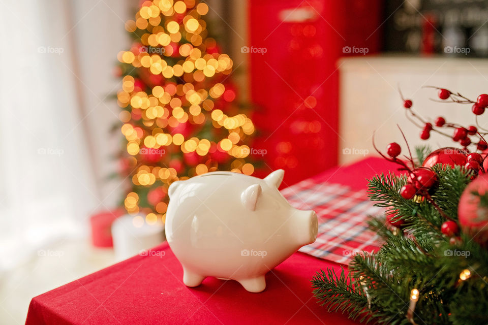 piggy bank with 100 dollars banknote in festive New Year atmosphere of scenery.  Magical bokeh with Christmas tree and bright lights.