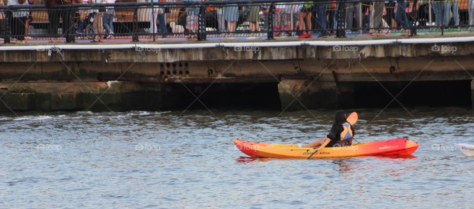 Woman paddling bright yellow and orange canoe on Hudson River on May evening