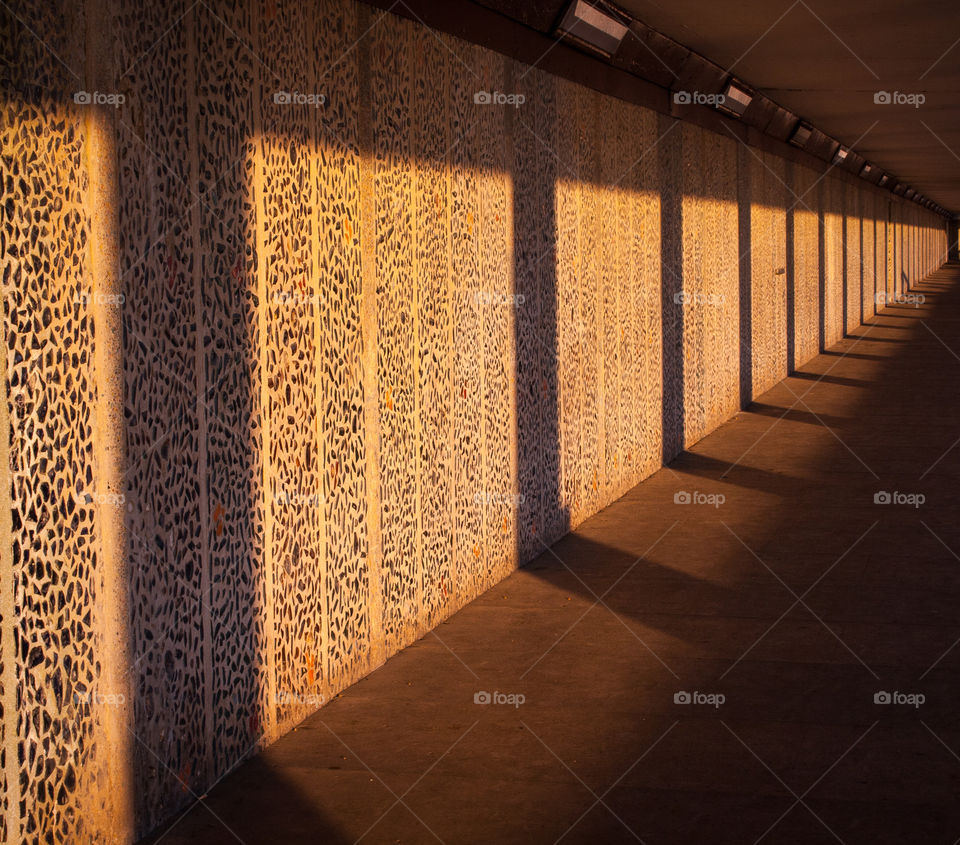 Long shadows are cast along an underground walkway, the walls a decorated with coloured glass