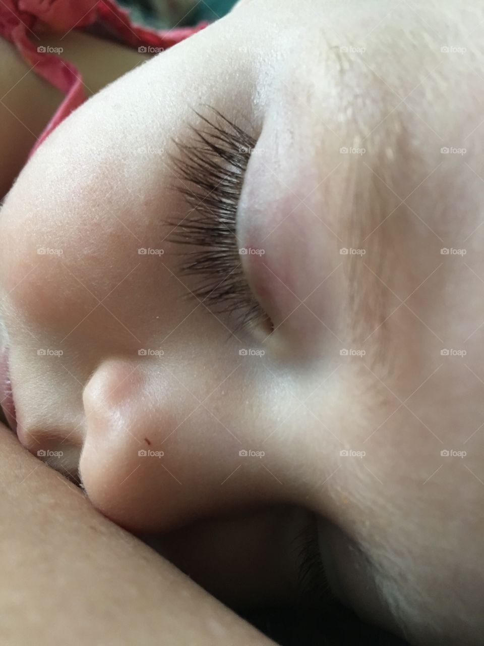 Close up of sleeping child snuggled into her mother’s arm.