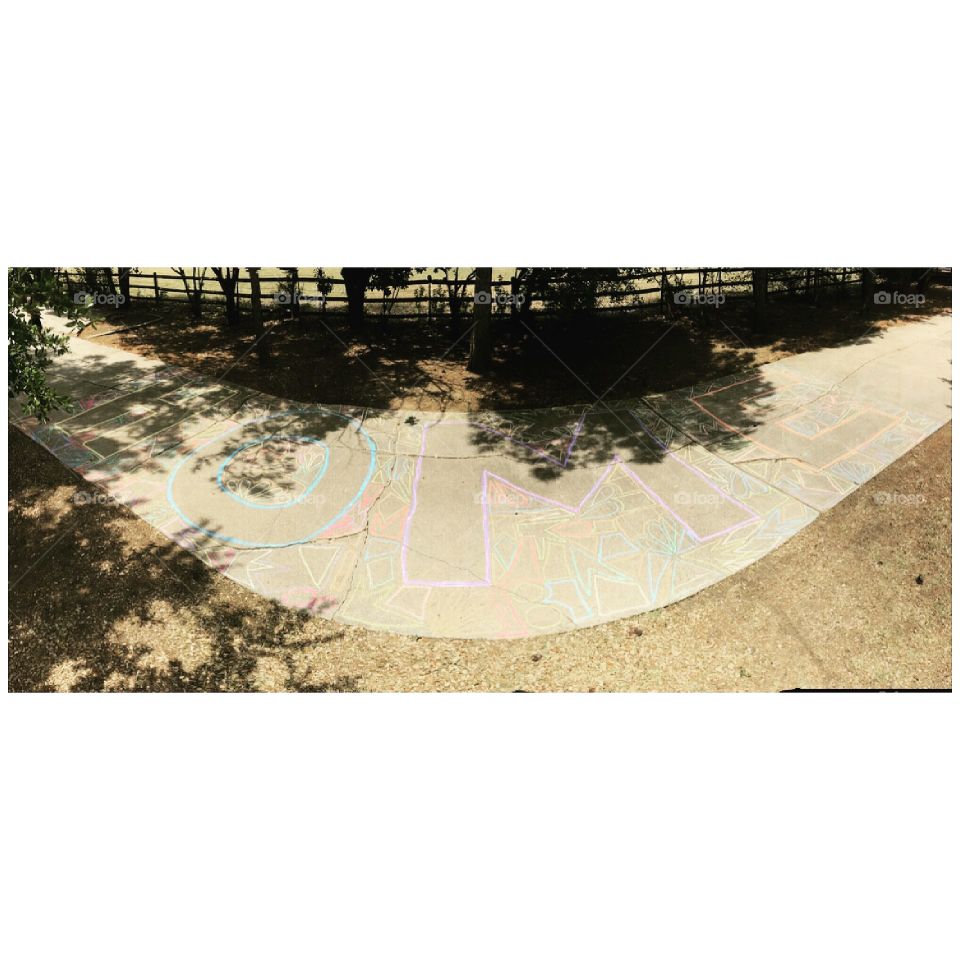 "home" written in all colors of chalk on a long driveway to a family home