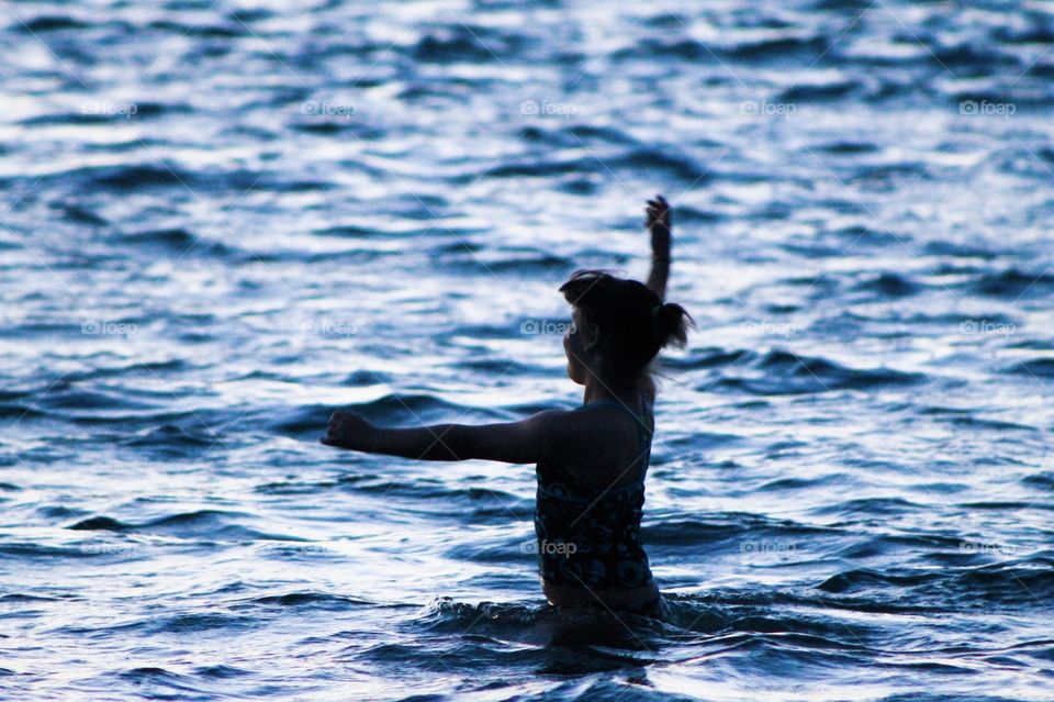 Silhouette of my middle daughter dancing in the inky blue ocean & smiling as she looks towards the light from the setting sun. Her outstretched arms & the profile of her face shows the joy she feels as she embraces the beauty of the moment. 
