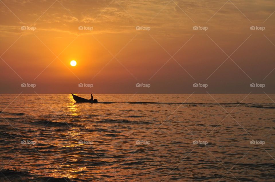 A boat passing the sea in the sunset, with some waves near the beach, and orange background.