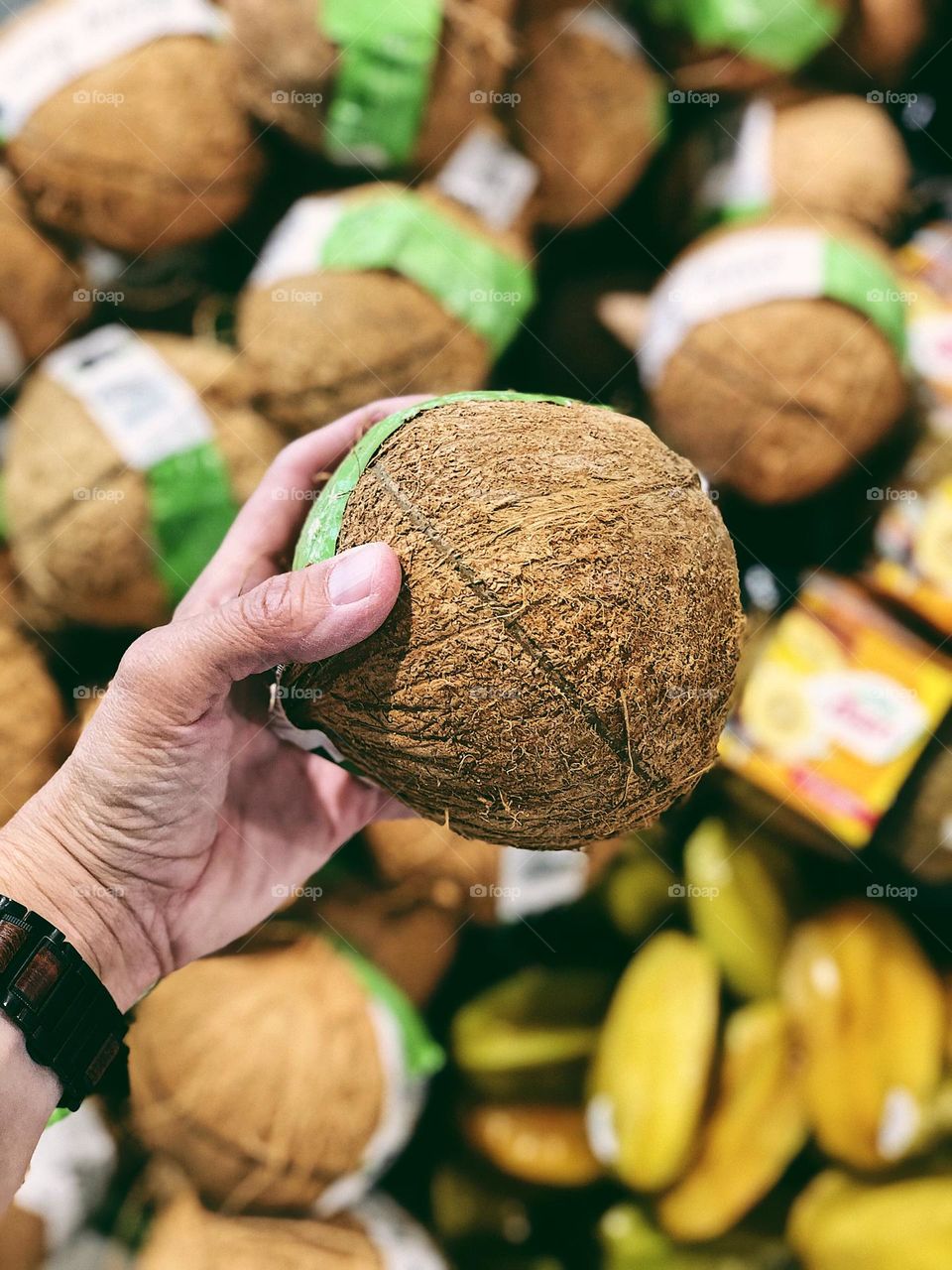 Coconuts in the grocery store, woman’s hand reaches for a coconut, shopping for produce in the store 