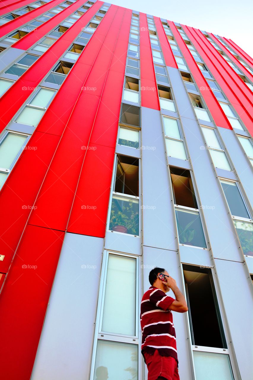 a man telephoning next to one red skyscraper
