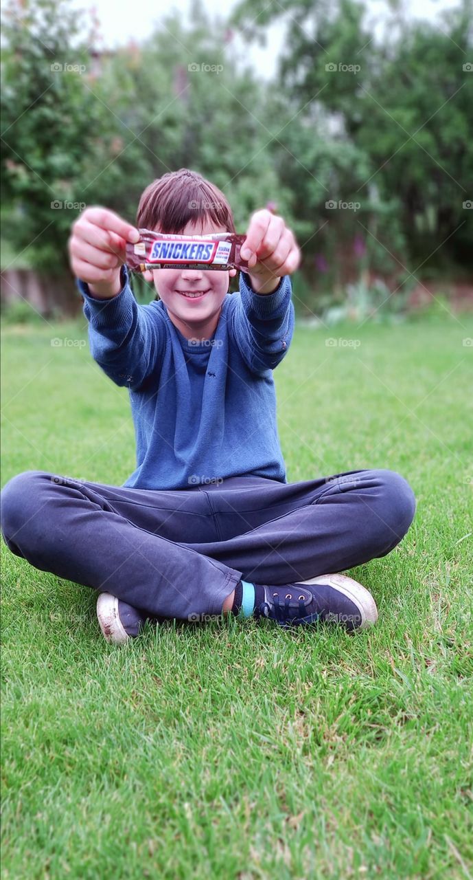 boy sitting on the grass and holding a snickers