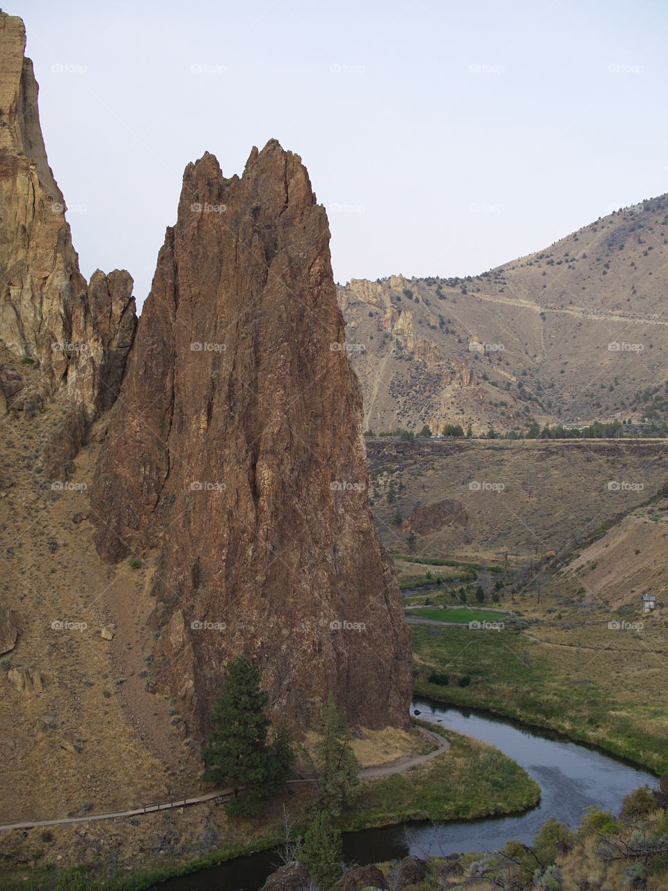 The rugged Smith Rocks and surrounding hills in Central Oregon with a trail at the bottom and the Crooked River winding around on an overcast summer day.