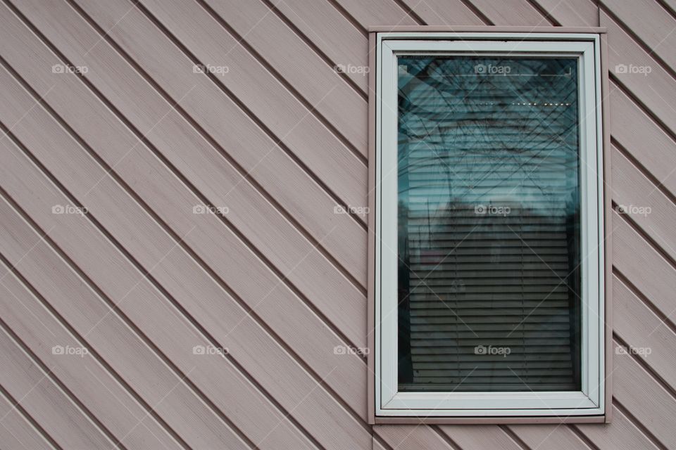 Exterior view of a solitary off center white-bordered window set against a wall of diagonal lines.