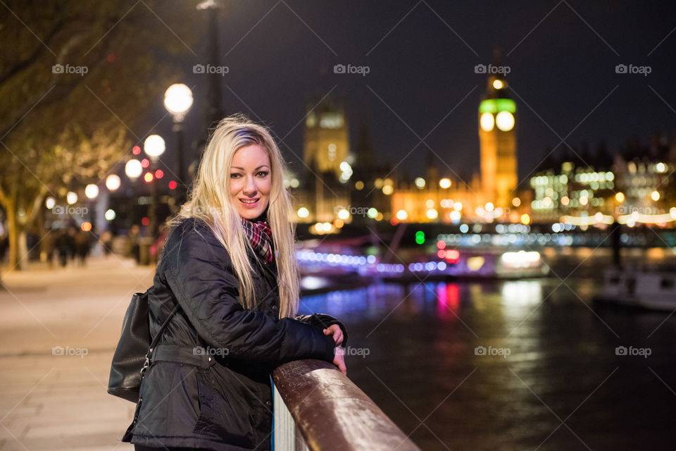 A woman of 30 years of age standing at a railing near Big Ben in London.