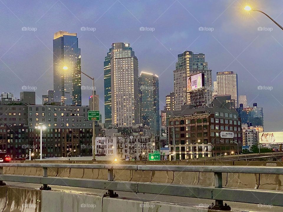 This is the view from the „Pulaski Bridge“ at „Newtown Creek“ in LIC, Queens walking from „Greenpoint“, Bklyn towards LIC in the twilight of upcoming nightfall. The skyscrapers pick up the last rays of the setting sun. 2023. Hypnotic Productions