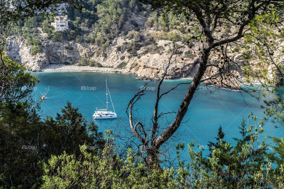 A yacht sat in the clear blue waters of Cala llonga bay in Ibiza. Mountains surround the bay with walks up both sides, giving good opportunities for photographers.