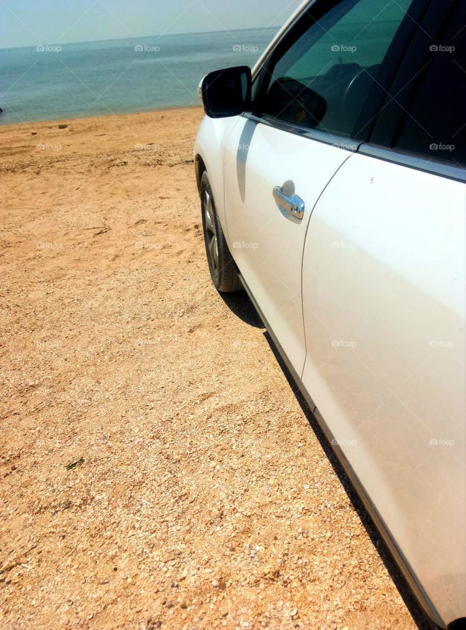 Sea.  Sandy beach and part of a white car.  Azure sea