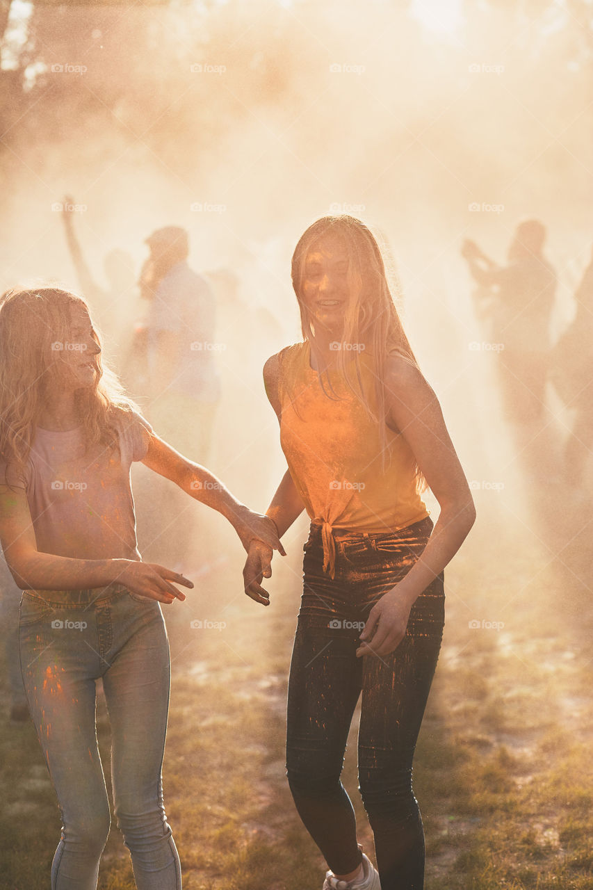 Portrait of happy smiling young girls with colorful paints on faces and clothes. Two friends spending time on holi color festival. Real people, authentic situations