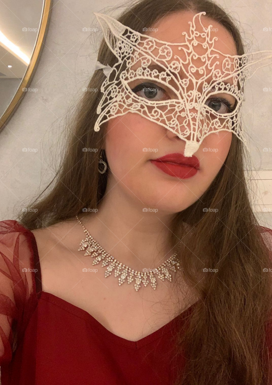 A girl in a Masquerade party putting on a mask and wearing jewellery