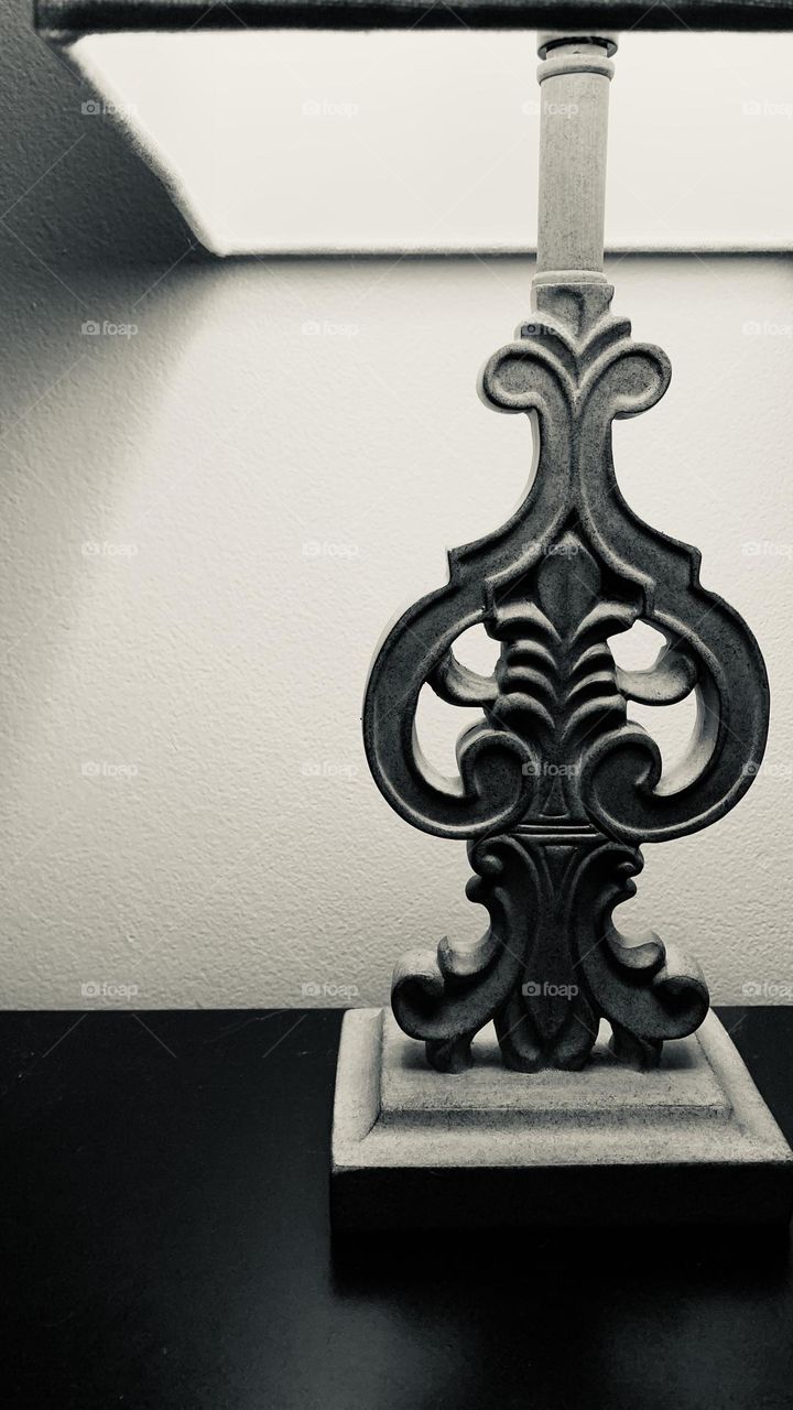 A unique desk lamp illuminates the night, it’s shadow reflecting against a blank wall. 