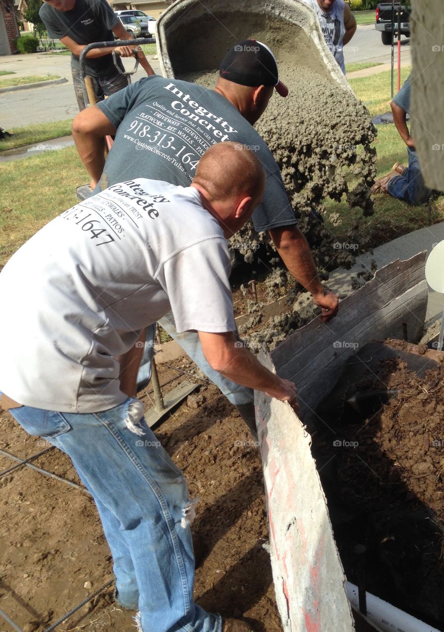 Men at work pouring concrete to construct a sidewalk.