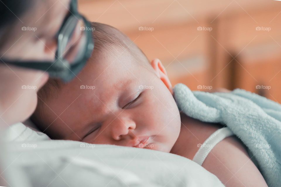 Cute sleeping caucasian baby in mother's arms lying on tummy, side view close-up. The concept of newborns, happy childhood, moms.