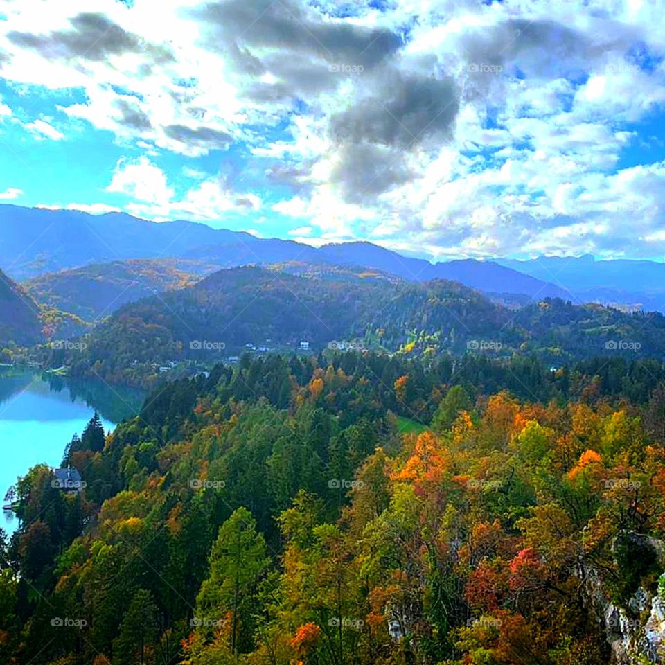 Forest.  The blue lake is surrounded by forested mountains.  Forest in autumn.  Above the autumn trees gray clouds through which the sun breaks