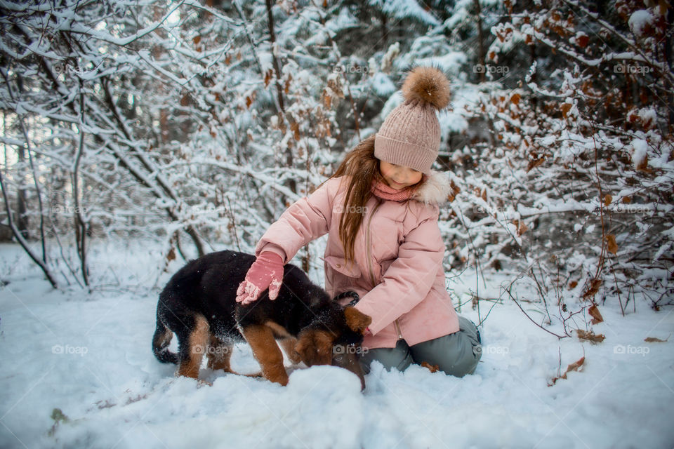 Little girl with German shepherd puppy in a winter park 