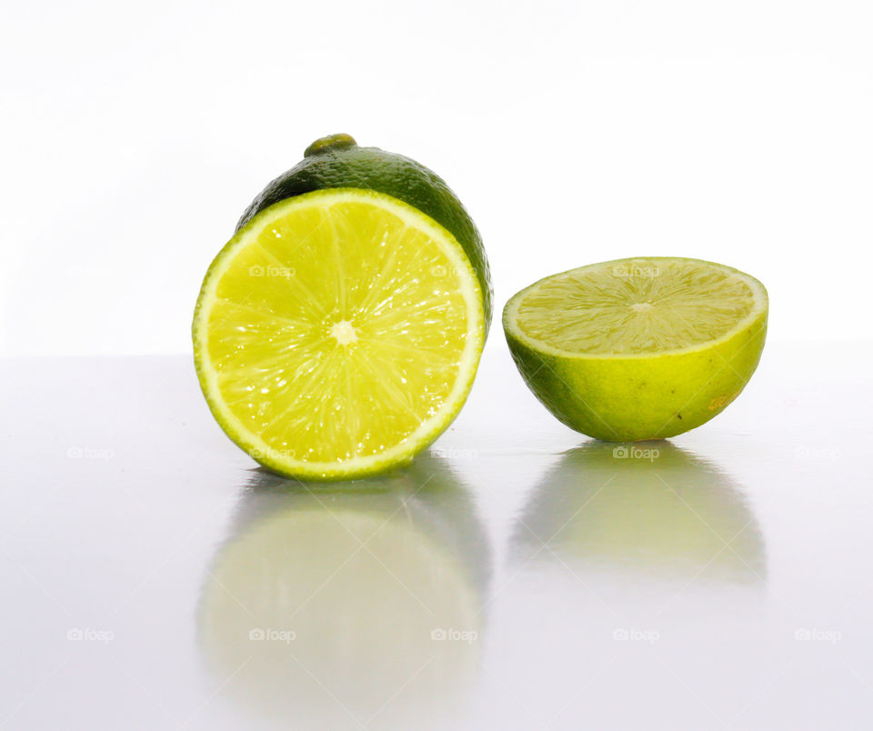 Limão Tahiti cortado em 2 partes sobre uma superfície branca e com fundo branco.