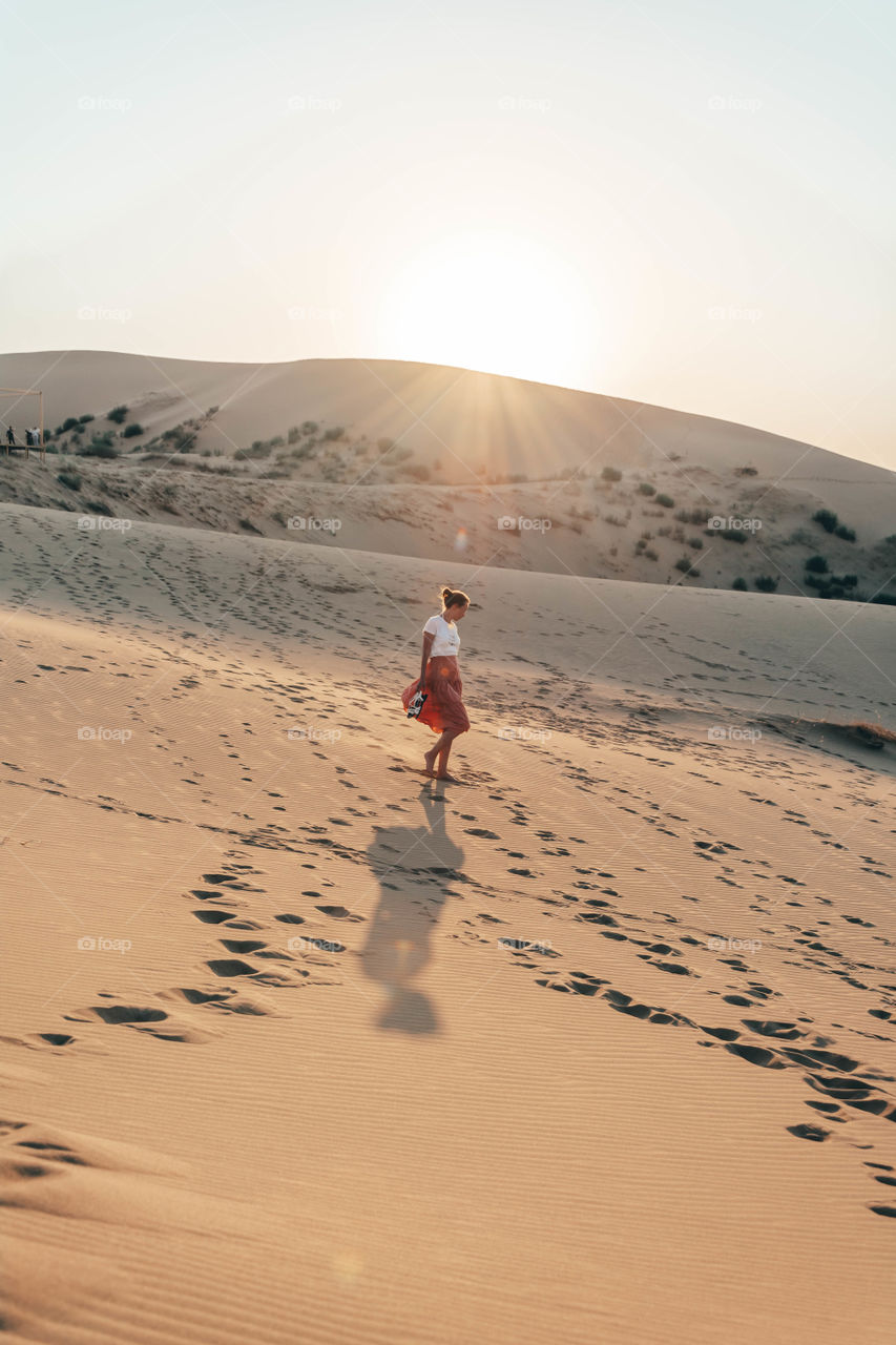 young woman walking among dunes at sunset