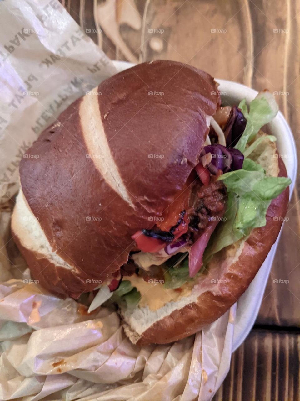 closeup of a vegetarian burger in a pretzel bun in paper on a wooden table. lettuce poking out the side