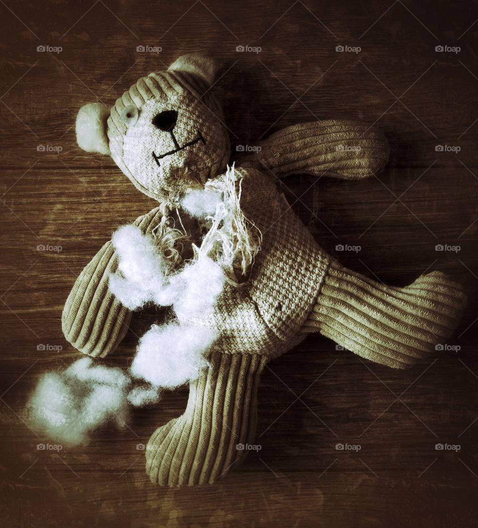 An old, abandoned teddy bear with his stuffing pulled out and laying, helpless on a wooden floor.
