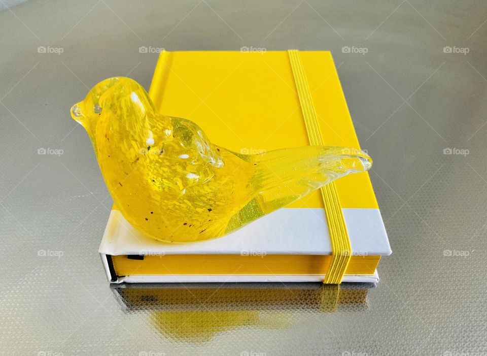 Yellow notebook and a whimsical glass figurine of a bird. 