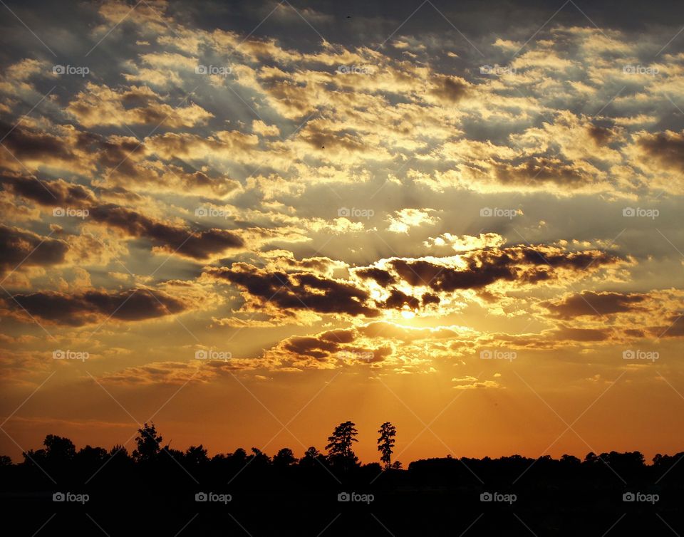 As the sun sets, the bright colors spread across the sky among the clouds.