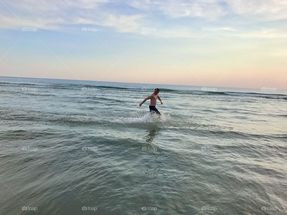 A man running through shallow water in the sea and enjoying his time by the ocean.