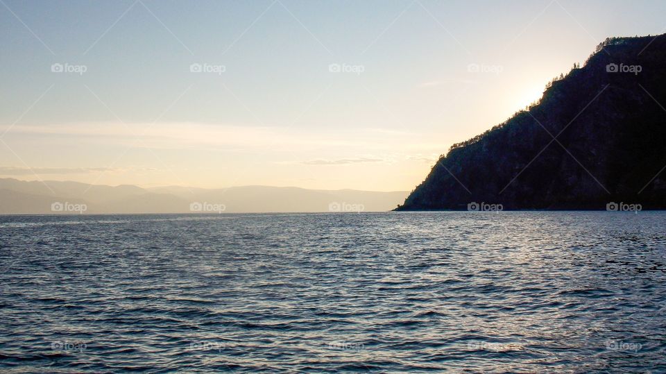 Trapezoid of the Eastern slope of the Seaside ridge. Khamar-Daban ridge on horizon in the sun rays of the passing day. The picture taken from the surfaces of the Bolshaya Krutaya Guba bay of lake Baikal.