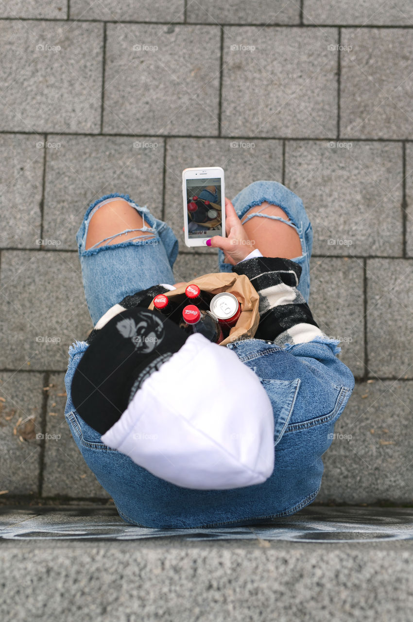 girl blogger sits on the street, looks at the phone, holds a package of Coca-Cola in her hands, top view. Flat lay 