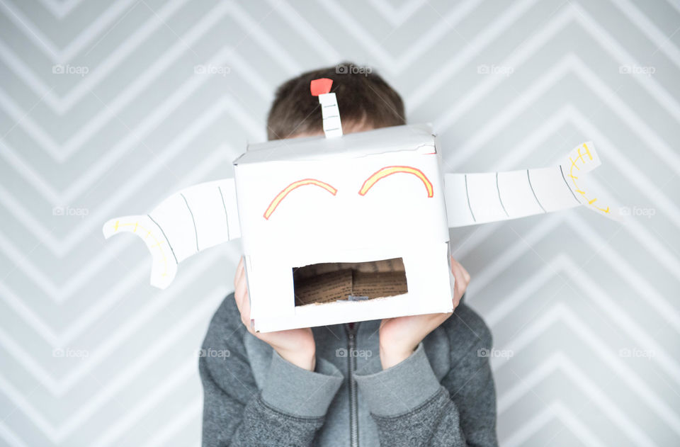 Young school aged boy holding up a handmade cardboard robot over his face