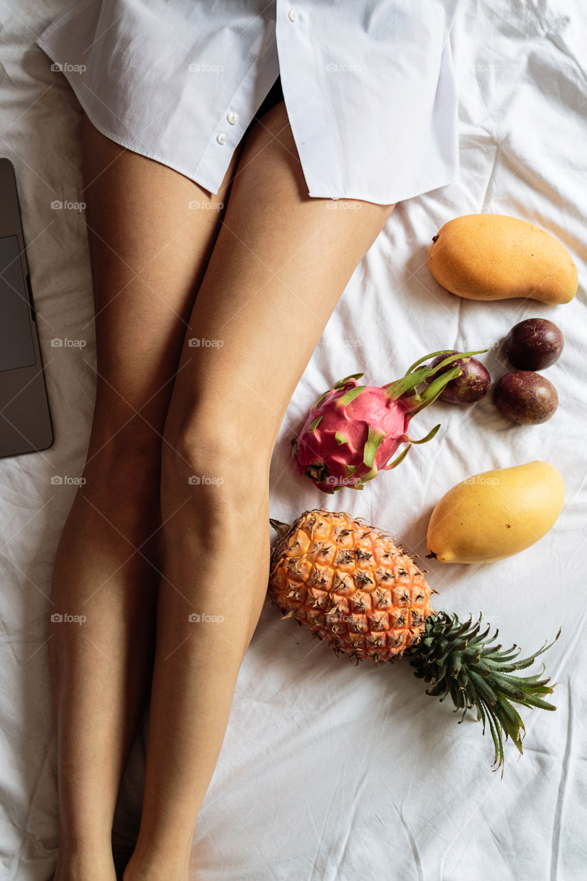 Woman legs and exotic fruits on the bed