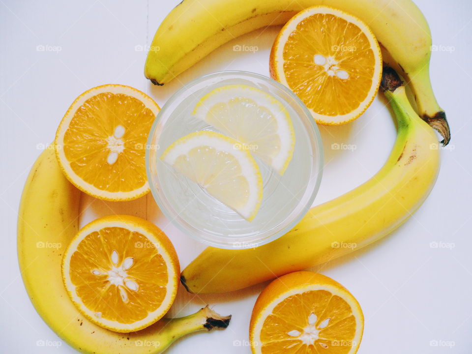 a glass of lemonade with lemon, bananas and sliced ​​oranges on a white background