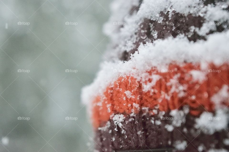 Snow on a brown and orange hat made of wool. Closeup with a blurry greenish background.