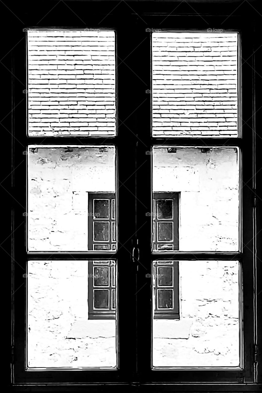 Black and white shot of a view on a vintage small-paned window through a vintage medium-paned window in Port-Louis